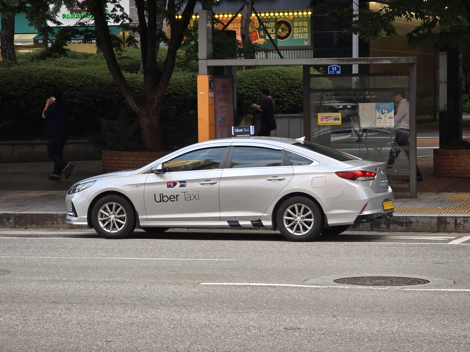 A white taxi in Korea displaying Uber Taxi branding and a roof light at the curb.