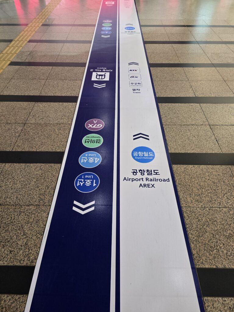Blue and white floor wayfinding line at Seoul Station pointing toward Airport Railroad AREX.