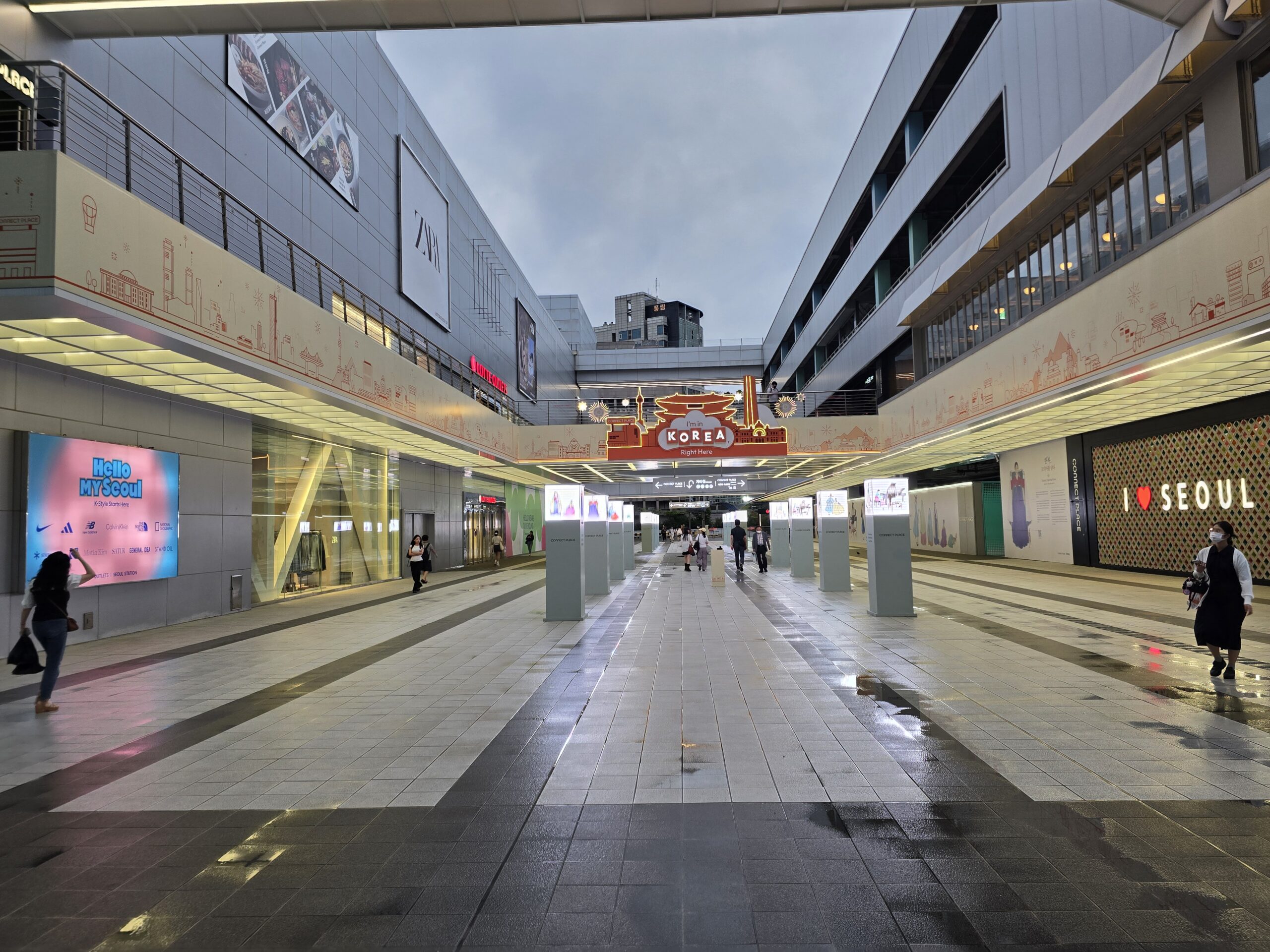 Wide Seoul Station Connect Place concourse with shops and travelers after rain.